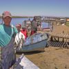 Fishers standing amongst beached boats, holding up bunches of fish at Velddrif with 'bokkom' — dried harders. Image by South Africa Tourism via Flickr (CC BY 2.0)
